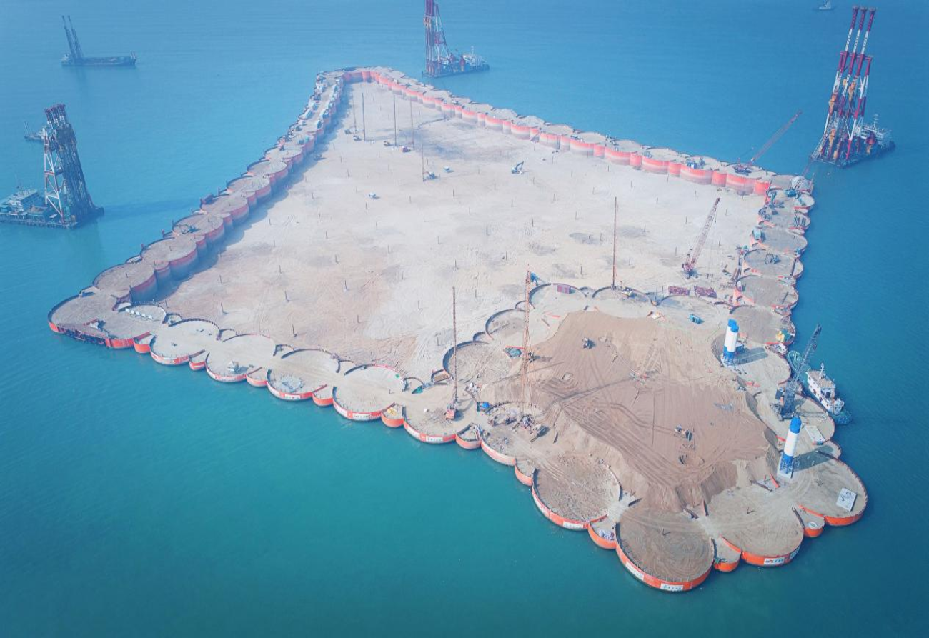 2016年12月28日，深中通道西人工島先行開建，這是深中通道工程在伶仃洋上落下的“第一子”，標(biāo)志著深中通道正式開工。西人工島島體采用菱形設(shè)計，形狀如同海上風(fēng)箏，是實現(xiàn)跨海橋梁和海底隧道轉(zhuǎn)換的關(guān)鍵。工程使用世界最大十二錘聯(lián)動液壓振動錘組，高精度振沉57個巨型鋼圓筒，歷時141天實現(xiàn)西人工島合龍，刷新了“外海快速成島”施工紀(jì)錄。圖為深中通道西人工島海上施工現(xiàn)場。